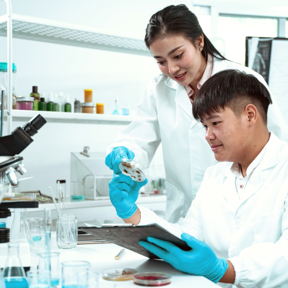 两位身穿实验服并佩戴防护手套的科学家正在观察一只培养皿，可能正在分析其中的样本或实验结果。